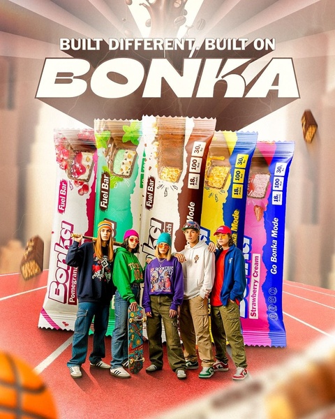 A group of young, stylish individuals standing on a basketball court behind a stacked display of flavored protein bars.